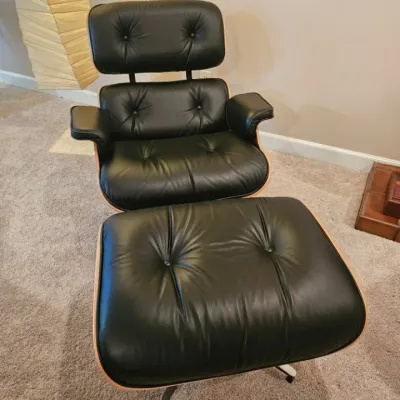 Eames lounge chair and matching ottoman in black leather upholstery with a molded plywood shell.