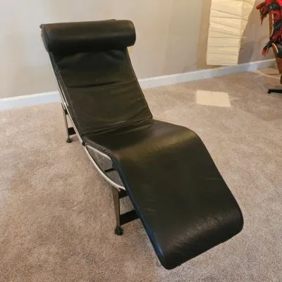 Le Corbusier style LC4 chaise lounge with black leather upholstery, matching headrest pillow, and a chrome tubular frame on a black base.