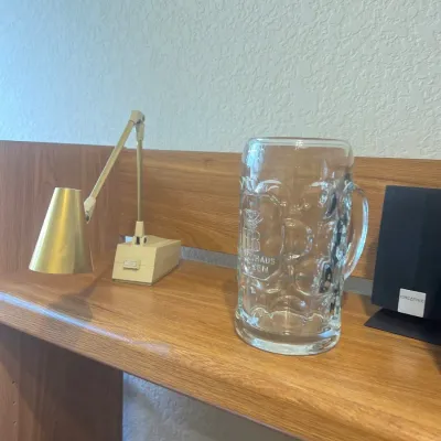 Vintage brass adjustable desk lamp alongside a Hofbräuhaus München dimpled glass beer stein on a wooden shelf.