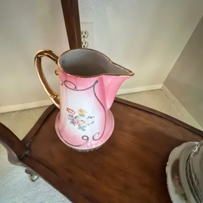 Vintage pink porcelain pitcher featuring hand-painted floral motifs and a gilt handle and trim