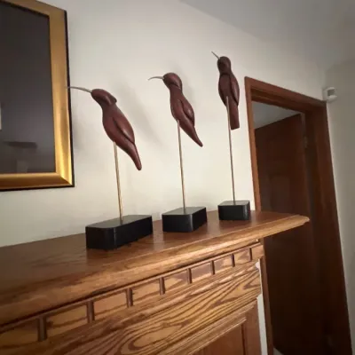 Trio of mid-century modern carved wooden bird sculptures on metal stands with black rectangular bases.