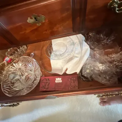 Open wooden dresser drawer filled with various vintage crystal glassware pieces, serving bowls, and a boxed item.