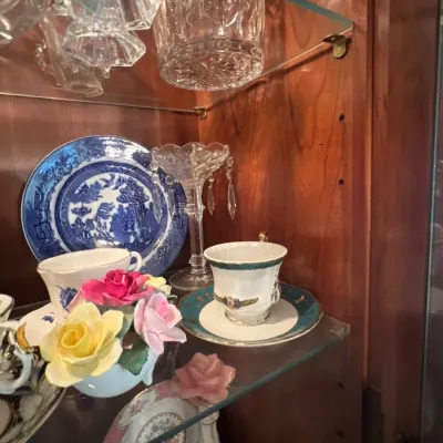 Collection of vintage porcelain and crystal glassware inside a wooden display cabinet, featuring a Blue Willow decorative plate, fine...