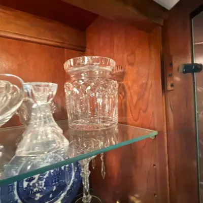 Collection of crystal glassware, including a cut crystal biscuit jar and candlesticks, displayed inside a wooden china cabinet alongside...