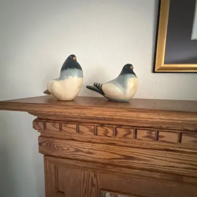 Pair of carved and painted wooden bird figurines displayed on an oak fireplace mantle.