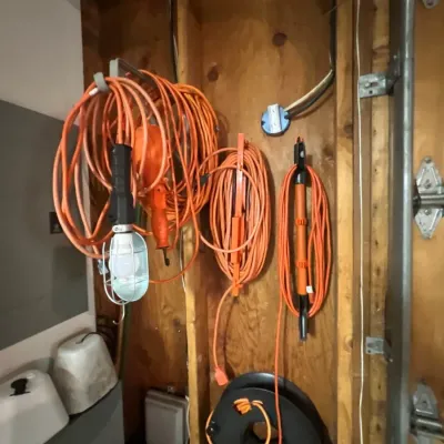 Assortment of heavy-duty orange extension cords, cord organizers, and a cage-protected drop light hanging on a workshop wall.