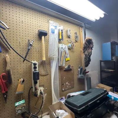 Workshop area featuring pegboard-mounted hand tools, zip ties, power strips, and a plastic toolbox on the workbench.