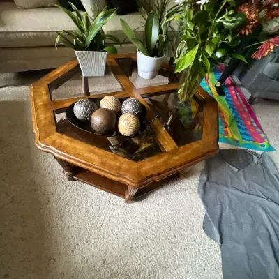 Hexagonal wood and glass coffee table displaying decorative orb centerpiece, potted houseplants, and a floral arrangement.