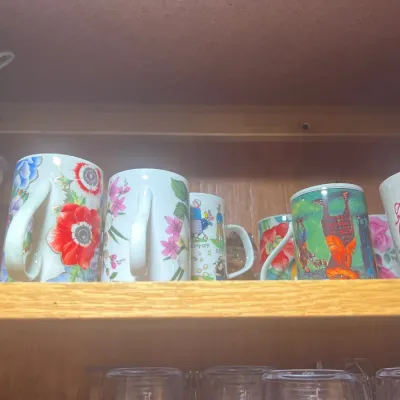 Collection of decorative ceramic coffee mugs featuring floral patterns, novelty illustrations, and holiday graphics stored on a wooden...