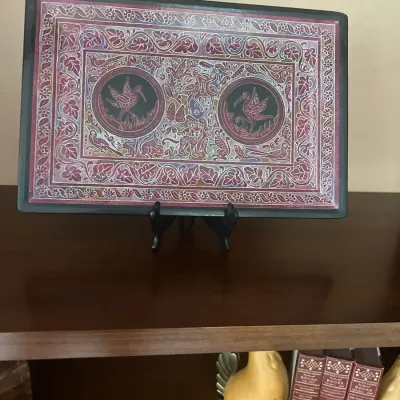 Hand-carved Olinalá lacquered wooden tray from Guerrero, Mexico, displayed on a stand. Features intricate etchings of birds, flora, and...
