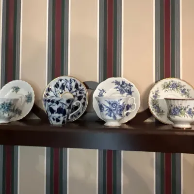Collection of four vintage porcelain teacups and matching saucers, featuring various blue floral patterns and gold trim, displayed on a...