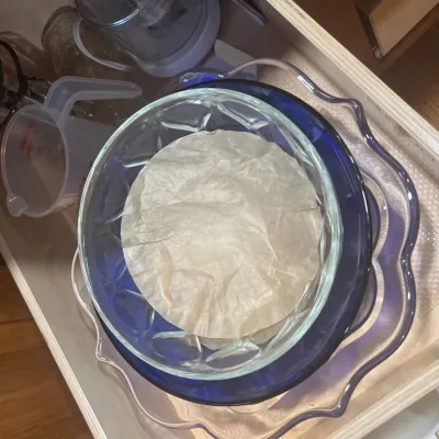 Collection of kitchenware stored in a cabinet drawer, including stacked glass serving bowls, plastic measuring cups, and a food processor...