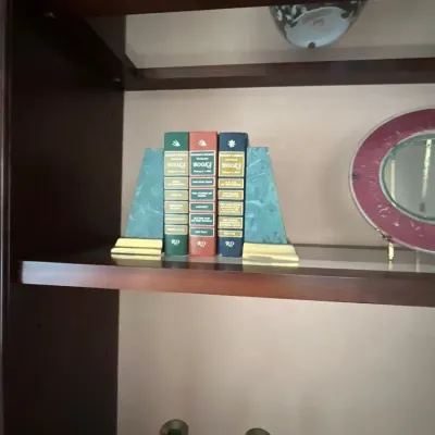 Set of three Reader's Digest Condensed Books held by faux-marbled bookends on a wooden shelf alongside a pair of brass candlesticks...