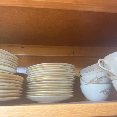Lenox collection of mid-century fine china dinnerware with gold rims and wheat stalk motifs, including stacked plates, saucers, and cups.