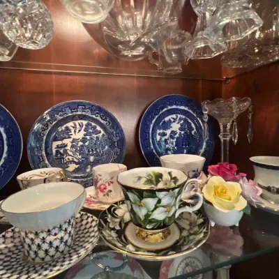 Collection of fine china teacups, saucers, and Blue Willow pattern decorative plates displayed inside a glass cabinet alongside cut...
