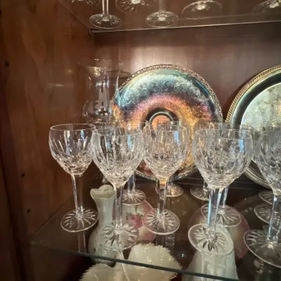 Collection of cut crystal wine glasses displayed inside a wooden cabinet alongside decorative silver-plated trays.