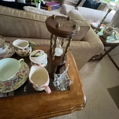 Collection of tabletop decor including an hourglass with brass and wood accents, floral china teacups and creamers, and a clear glass...