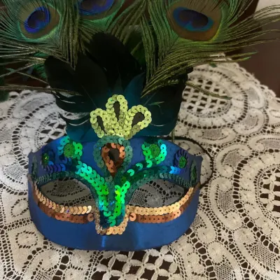 Venetian-style masquerade mask featuring blue fabric, iridescent sequin trim, and peacock feather plumage.