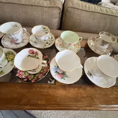 Collection of assorted vintage porcelain tea cups and matching saucers featuring floral motifs and gold rim details displayed on a table.