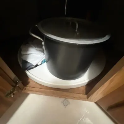 Large dark metal stock pot with a fitted lid, resting inside a corner Lazy Susan cabinet.