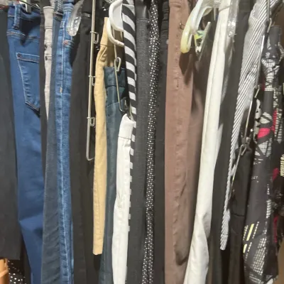 Closet rod filled with an assortment of women's pants, including blue denim jeans, khaki trousers, and patterned slacks on plastic...