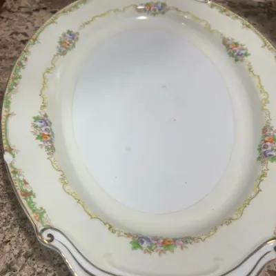 Vintage oval porcelain serving platter featuring a delicate floral motif, cream border, and gilt filigree rim accents.