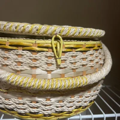 Vintage round woven sewing basket in yellow and cream tones, featuring a loop closure and thick wrapped handle.