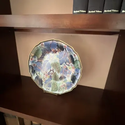 Vintage Japanese chokin decorative plate featuring detailed floral and leaf motifs with gold accents, displayed on a dark wood bookcase...