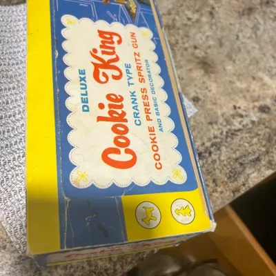 Vintage Deluxe Cookie King crank-type cookie press and spritz gun in its original yellow and blue box.