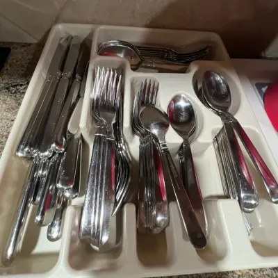 Large set of modern stainless steel flatware, including knives, forks, and spoons, organized in a plastic drawer tray.