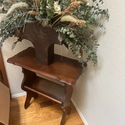 Vintage dark stain wooden accent table with lower trough shelf, topped with a rustic decorative vessel holding a large dried botanical...