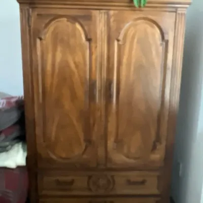 Traditional wooden armoire featuring double raised-panel doors above two lower drawers with carved accent detailing.
