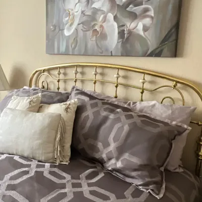 Brass queen headboard with spindle accents, staged with geometric patterned bedding and a large floral canvas print above.