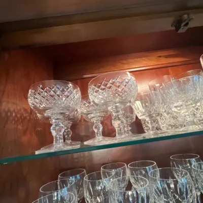 Collection of crystal glassware including cut-glass coupe goblets and wine stems displayed inside a illuminated wooden cabinet shelf.