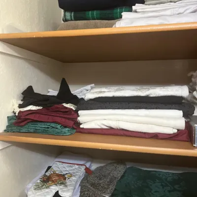 Assorted household linens, towels, table runners, and oven mitts neatly stacked on wooden closet shelves.