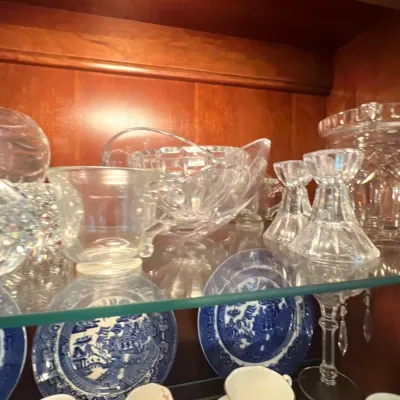 Collection of crystal glassware, including candlesticks, cups, and a handled basket bowl, displayed alongside blue-and-white porcelain...