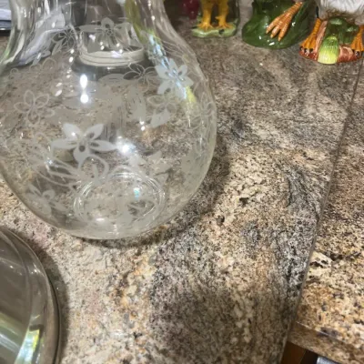 Vintage clear glass pitcher with etched floral detailing, shown alongside ceramic rooster figurines on a countertop.