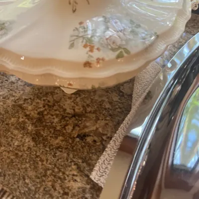 Vintage ceramic covered tureen featuring delicate floral patterns and gilt accents, shown alongside a polished silver-tone serving tray.