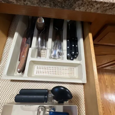 Kitchen drawer containing an assortment of flatware, steak knives, a can opener, and bottle opener organized in plastic trays.