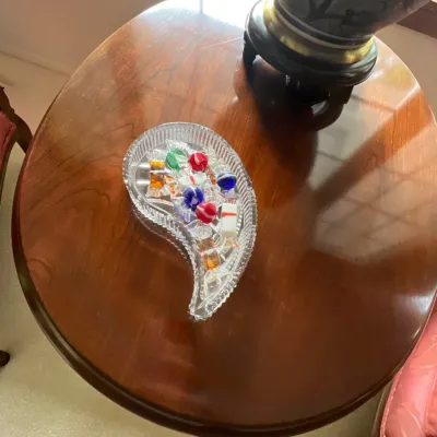 Vintage paisley-shaped cut crystal candy dish filled with decorative glass candies, displayed on an oval cherry wood side table.