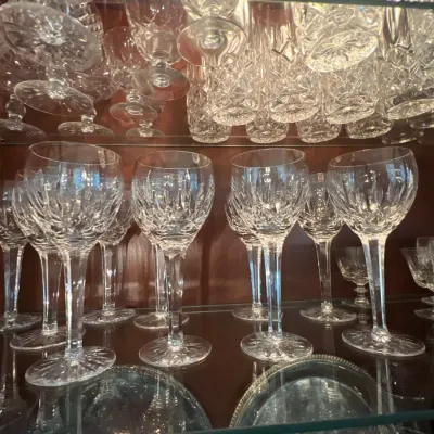 Collection of crystal stemware and glassware displayed on glass shelves inside a wooden cabinet.