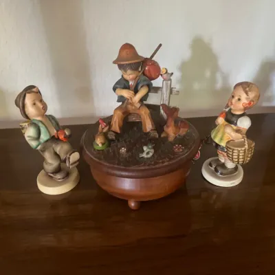Collection of three vintage Hummles, including two Goebel-style children and a central carved wooden music box depicting a boy playing a...
