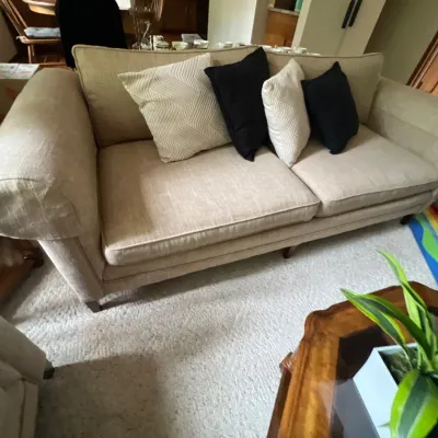 Contemporary beige upholstered sofa featuring rolled arms and dark tapered wooden legs, styled with contrasting black and patterned throw...
