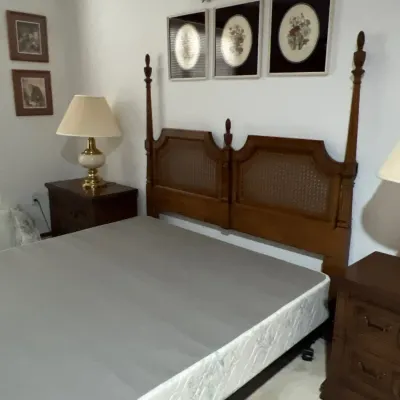 Traditional wooden four-poster bed frame featuring woven cane inserts in the headboard, flanked by matching dark wood nightstands.