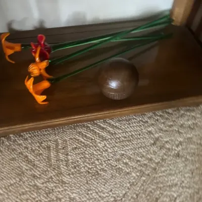 Collection of vibrant blown glass flower stems in orange and red hues, displayed in a wooden rack alongside a dark wooden sphere.