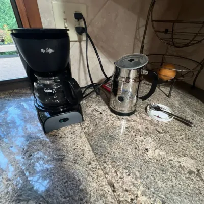 Black Mr. Coffee 4-cup drip coffee maker alongside a stainless steel electric milk frother on a granite countertop.