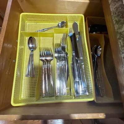 Set of stainless steel flatware organized inside yellow plastic drawer trays, featuring knives, forks, and spoons.