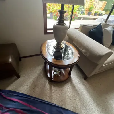 Traditional wooden oval end table with a mirrored glass insert top, accompanied by a ceramic and brass table lamp with a pleated shade.