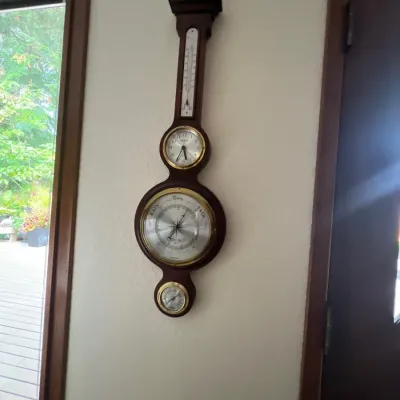 Vintage wood banjo-style weather station featuring a thermometer, clock, barometer, and hygrometer with brass bezel accents.