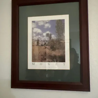 Framed Claude Monet exhibition poster featuring an impressionist landscape scene, housed in a dark wooden frame with double matting.